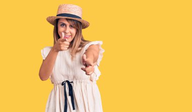 Yazlık şapkalı ve tişörtlü genç ve güzel bir kadın kamerayı mutlu ve komik yüzüyle işaret ediyor. iyi enerji ve titreşimler. 