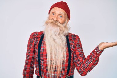 Gri saçlı, uzun sakallı, hippi görünümlü, neşeli yüzlü, eli kameraya bakan yaşlı bir adam.. 