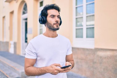 Şehirde akıllı telefon ve kulaklık kullanan ciddi bir suratı olan genç bir İspanyol..