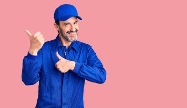 Orta yaşlı, tamirci üniforması giyen yakışıklı bir adam arka tarafı işaret ediyor. 