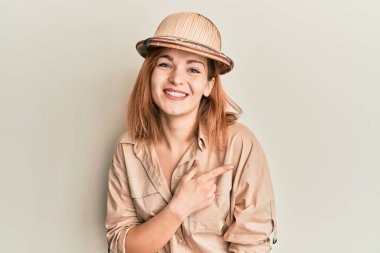 Kafkasyalı genç kadın kaşif şapkası takıyor. Gülümsüyor, eli ve parmağı yana doğru uzanıyor. 