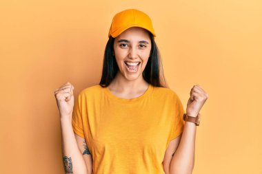 Teslimat üniforması ve şapka giyen genç İspanyol kadın kollarını kaldırıp gözleri açık bir şekilde başarıyı kutluyor ve şaşırıyor. Kazanan konsept. 