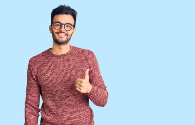 Kışlık süveter giyen ve gözlük takan genç, yakışıklı İspanyol adam elleriyle mutlu bir jest yapıyor. Kameraya bakıp başarıyı gösteren ifade. 