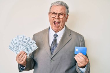 Yaşlı, gri saçlı, takım elbiseli, kredi kartı ve dolar tutan öfkeli, sinirli ve öfkeli bir adam. Öfkeyle bağırıyor. öfke ve agresif konsept. 