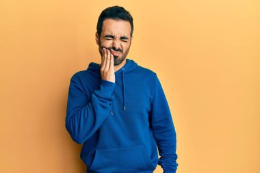 Günlük kıyafetler giyen genç İspanyol adam diş ağrısı ya da diş hastalığından dolayı acı dolu bir ifadeyle ağıza dokunuyor. dişçi 