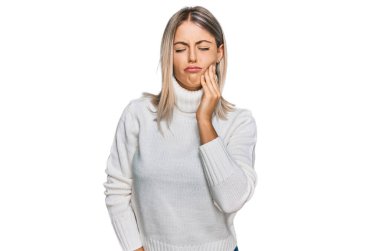 Balıkçı yaka kazak giyen güzel sarışın kadın diş ağrısı ya da diş hastalığından dolayı acı dolu bir ifadeyle ağzına dokunuyor. dişçi 