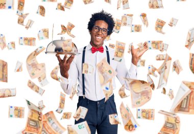 Yakışıklı Afro saçlı, garson üniforması giyen, elinde gümüş tepsiyle zaferi kutlayan gülümseyen ve kazanan yüz ifadesiyle elini kaldıran Afro-Amerikan bir adam.