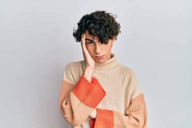 Latin kökenli genç adam sıradan bir kazak giyip kollarını kavuşturup depresyondan sıkılmış ve yorgun görünüyor.. 