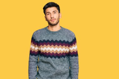 Kış süveteri giyen genç yakışıklı adam yüzünde ciddi bir ifadeyle rahatlamış. Basit ve doğal bir şekilde kameraya bakıyorsun.. 