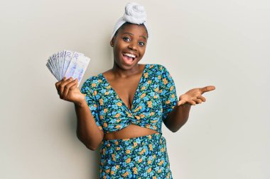 Kıllı türban takan genç Afrikalı bir kadın elinde 20 İsveç kronu banknotuyla başarıyı mutlu bir gülümsemeyle ve kazanan ifadeyle el kaldırarak kutluyor. 