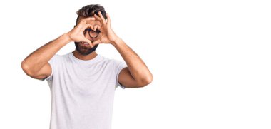 Gündelik kıyafetler ve gözlük takan genç İspanyol adam kalp şeklinde el ve parmakları ile tabelanın içinden bakıp gülümsüyor. 