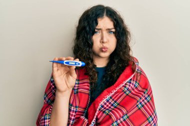 Battaniyeye sarılı kıvırcık saçlı esmer bir kadın termometre tutarak komik yüzüyle yanaklarını şişiriyor. Ağzı havayla şişer, havayı yakalar.. 