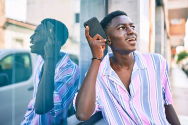 Genç Afrikalı Amerikalı gülümseyen adam şehrin caddesindeki akıllı telefonda mutlu bir şekilde konuşuyor..