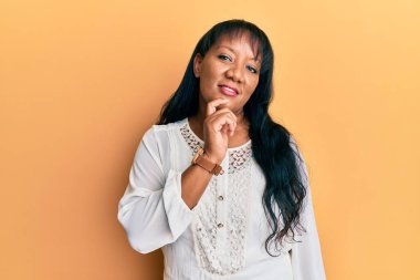 Orta yaşlı Afro-Amerikalı kadın, günlük kıyafetler giyip kameraya kollarını kavuşturup, çenesini kapatarak gülümsüyor. Olumlu düşünmek. 