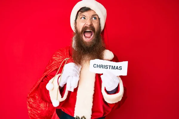 英俊的红头发男子 留着长胡子 身穿圣诞老人服装 手里拿着圣诞短信 怒气冲冲地尖叫着 怒气冲冲地大叫着 愤怒和好斗的概念 — 图库照片