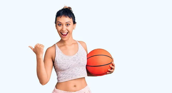 Młoda Kobieta Trzyma Piłkę Koszykówki Wskazując Kciuk Góry Bok Uśmiechając — Zdjęcie stockowe