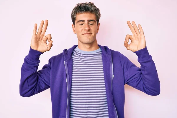 年轻英俊的男子穿着宽松的紫色运动衫 闭眼笑着 用手指做冥想动作 瑜伽概念 — 图库照片
