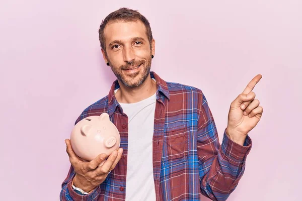 Young Handsome Man Holding Piggy Bank Smiling Happy Pointing Hand — Stock Photo, Image