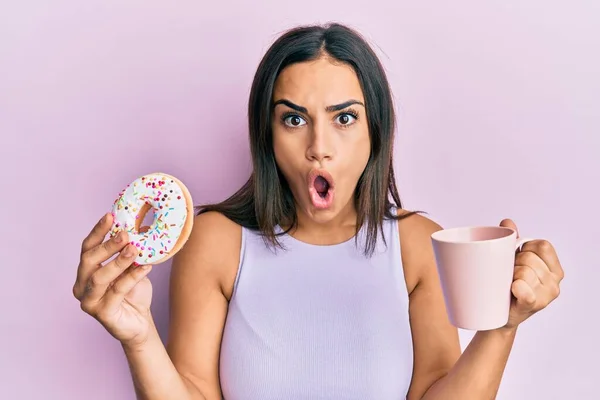 Joven Morena Comiendo Donut Bebiendo Café Asustada Sorprendida Con Expresión —  Fotos de Stock