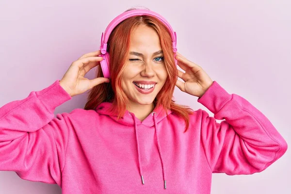 Mujer Pelirroja Joven Escuchando Música Usando Auriculares Guiñando Ojo Mirando — Foto de Stock