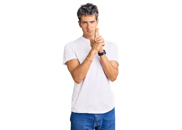 Young handsome man wearing casual white tshirt holding symbolic gun with hand gesture, playing killing shooting weapons, angry face