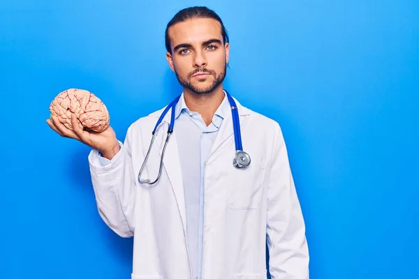 Jovem Bonito Homem Vestindo Médico Casaco Segurando Cérebro Pensando Atitude — Fotografia de Stock