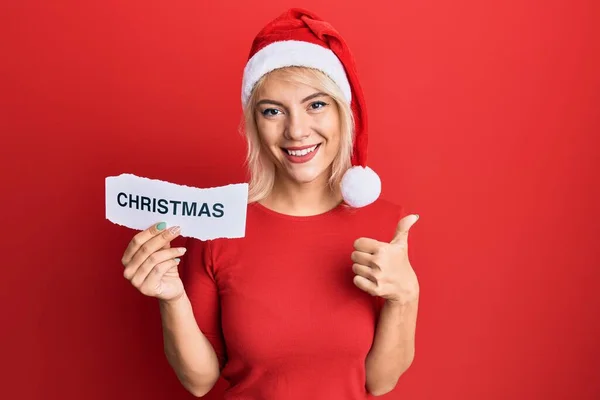Junges Blondes Mädchen Mit Weihnachtsmütze Hält Papier Mit Weihnachtswort Und — Stockfoto