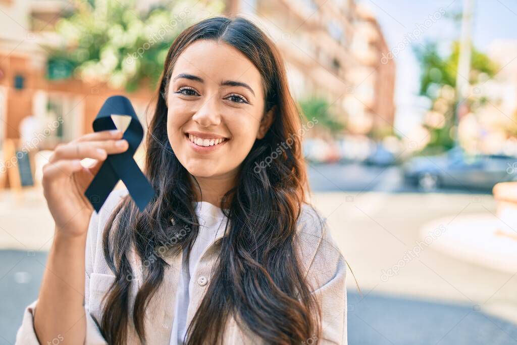 Young hispanic woman smiling happy holding black ribbon at the city.