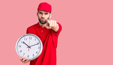 Genç, sakallı, teslimat üniformalı, büyük saati tutan, kamerayı işaret eden yakışıklı bir adam. Ve sen, kendinden emin, ciddi görünüyorsun. 