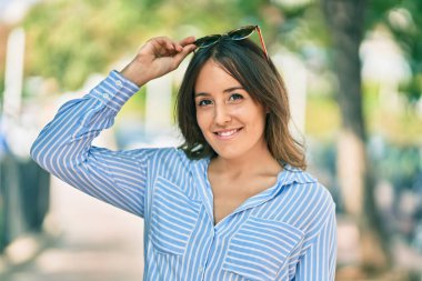 Genç İspanyol kadın gülümsüyor. Parkta güneş gözlüğüne dokunduğu için mutlu..