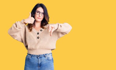 Güzel, genç, esmer, günlük kıyafetler giyen, gözlüklü, baş parmak kaldıran, fikir ayrılığı ve anlaşma ifadesi olan bir kadın. çılgın çatışma 