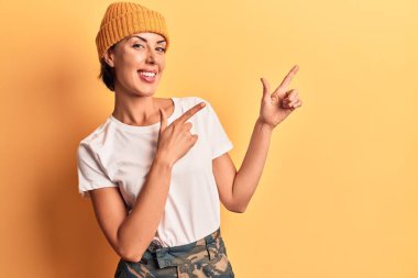 Yün şapkalı güzel bir kadın gülümsüyor ve kameraya bakıyor iki eliyle ve parmaklarıyla kenarı işaret ediyor.. 