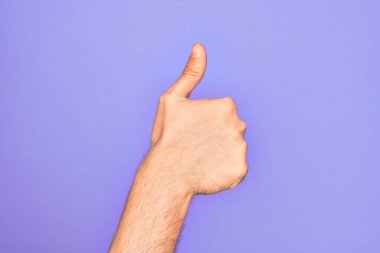 İzole edilmiş mor arka planda parmaklarını gösteren beyaz bir gencin eli başarılı bir onay jesti yapıyor. Başparmaklar yukarı, onaylama ve pozitif sembol ile.