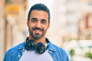 Şehirde kulaklık takarak mutlu gülümseyen genç İspanyol adam..