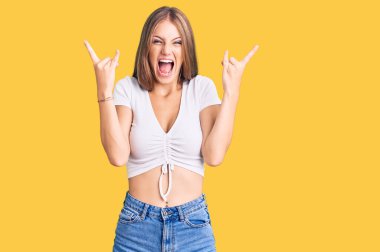 Genç, güzel, sarışın, günlük beyaz tişörtler giyen çılgın bir ifadeyle bağıran, elleri havada rock sembolü yapan bir kadın. Müzik yıldızı. ağır müzik konsepti. 