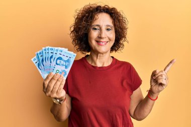 Güzel orta yaşlı bir kadın elinde 10 yuan Çin banknotları tutarken mutlu bir şekilde elini ve parmağını kenarı işaret ediyor. 