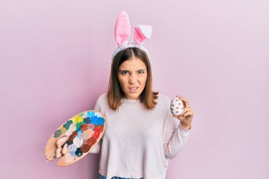 Paskalya tavşanı kulaklı, elinde palet, yumurtadan bihaber ve kafası karışık bir ifade olan genç ve güzel bir kadın. şüphe kavramı. 