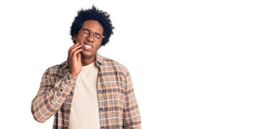 Yakışıklı Afro saçlı, günlük kıyafetler giyen, gözlüklü, diş ağrısı ya da diş ağrısı yüzünden ağıza dokunan ve acı veren bir ifadeyle dokunan Afro-Amerikan erkeği. dişçi 