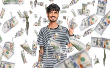 Gündelik kıyafetler giyen, gülümseyen ve kameraya göz kırpan genç İspanyol adam zafer işareti yapıyor. İki numara..