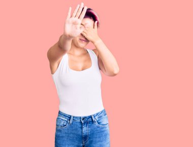 Pembe saçlı, sıradan kıyafetler giyen, elleriyle gözleri kapayan, üzgün ve korku dolu hareketler yapan genç ve güzel bir kadın. utangaç ve olumsuz kavram. 