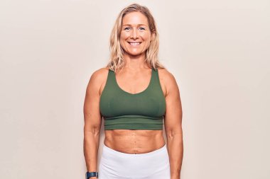 Orta yaşlı, beyaz, sarışın, spor giyimli, yüzünde mutlu ve havalı bir gülümseme olan bir kadın. şanslı kişi. 