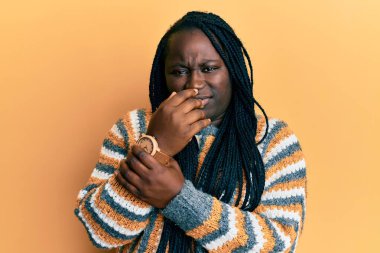 Saçları örgülü genç siyah bir kadın günlük kazak giyiyor. Ellerinde ve parmaklarında ağrı var. Eklem iltihabı var. 