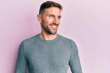 Sakallı, sıradan bir kazak giyen, rahat bir görünüm takınan, kendine güvenen ve gülümseyen yakışıklı bir adam.. 