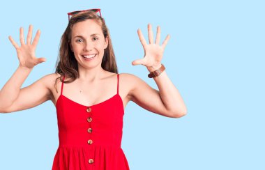 Genç, güzel, sarışın bir kadın gündelik elbiseler giyer ve parmaklarıyla on numarayı gösterir ve gülümserken kendinden emin ve mutludur.. 