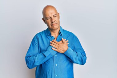 Orta yaşlı, kel, sıradan kıyafetler giyen, elleri göğsünde gülümseyen, gözleri kapalı, yüzünde minnet ifadesi olan bir adam. sağlık kavramı. 