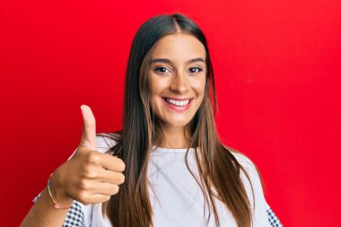 Neşeli ve pozitif gülümseyen Latin kökenli genç bir kadın. Başparmağıyla mükemmel ve onay işareti yapıyor. 