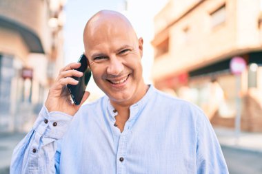 Orta yaşlı kel adam gülümsüyor. Şehirdeki akıllı telefondan mutlu mesut konuşuyor..