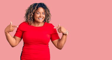 Genç Afro-Amerikan artı cüsseli kadın günlük kıyafetler giyiyor. Kendine güvenen, yüzünde gülümseme olan, kendini gururlu ve mutlu gösteren bir kadın.. 