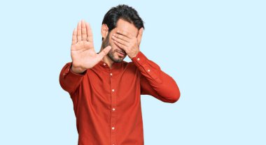 Latin kökenli genç bir adam, günlük kıyafetler giyip, elleriyle gözlerini kapatıyor ve üzgün ve korku ifadeleriyle jestleri durduruyor. utangaç ve olumsuz kavram. 