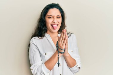 Katolik tespihiyle oynayan güzel İspanyol kadın komik bir ifadeyle mutlu bir şekilde dilini dışarı çıkarıyor.. 